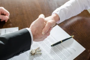 agent shaking hands with client over signed contract