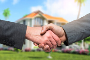 Close up of two people shaking hands with house in background